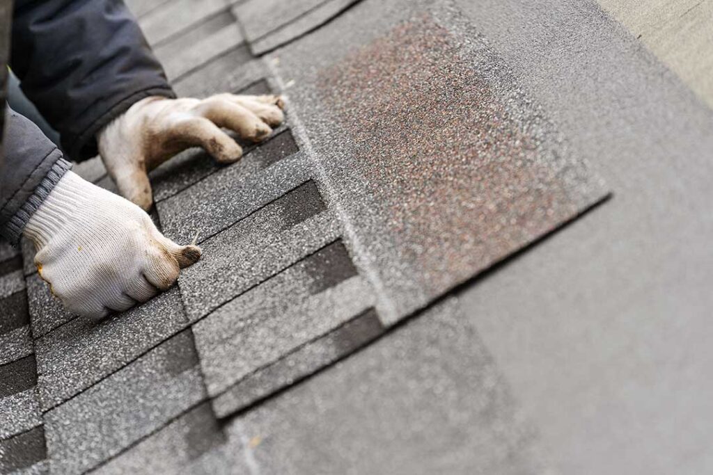 Homeowner reviews roof damage photos and insurance papers beside a window during winter weather.