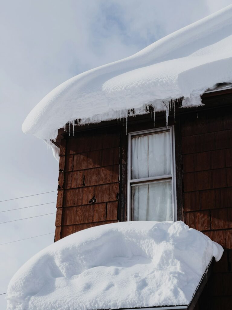Snow-covered house roof with an ice dam along the eaves and icicles hanging above the gutter.