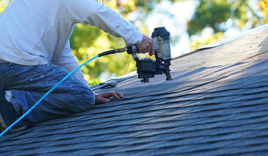 Homeowner inspecting ceiling stains and attic roof boards with a flashlight after a storm.